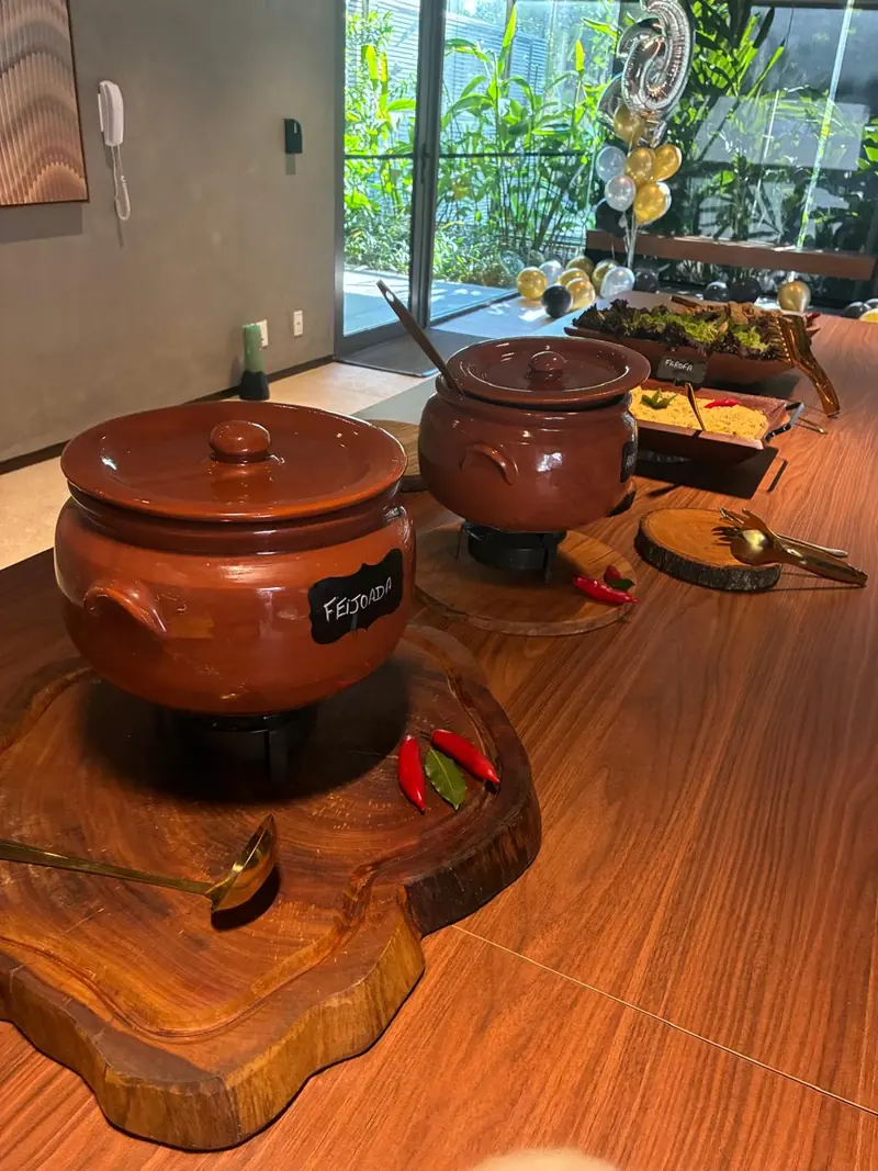 Panelas de barro com feijoada sobre tábua de madeira rústica, decoradas com pimentas vermelhas