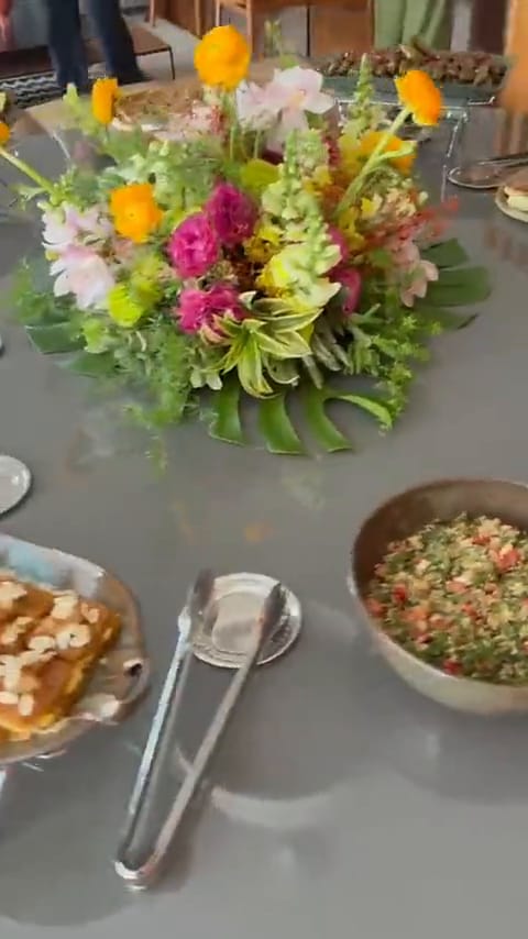 Buffet árabe montado de dia, com arranjo de flores coloridas e pratos sobre réchauds